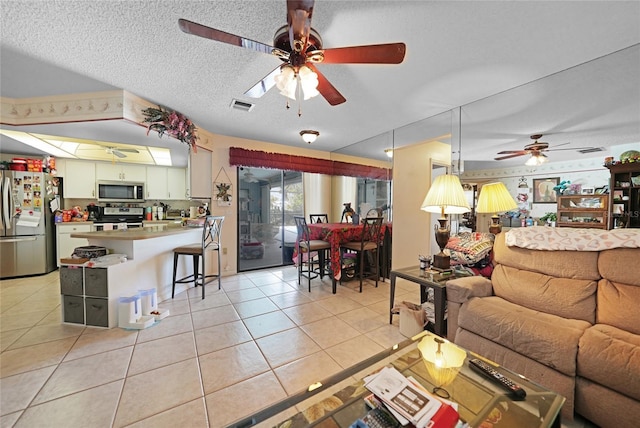 living room featuring light tile patterned floors, ceiling fan, visible vents, and a textured ceiling