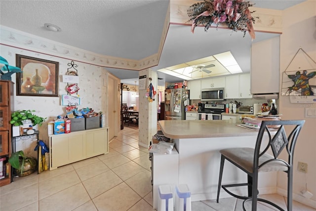 kitchen with light tile patterned floors, stainless steel appliances, a ceiling fan, a peninsula, and wallpapered walls