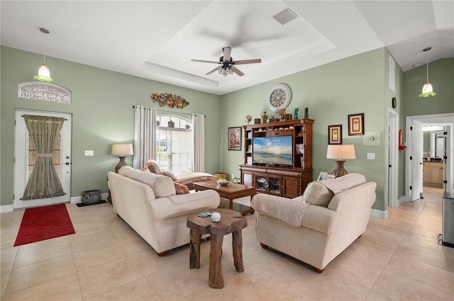 living room with a tray ceiling, light tile patterned floors, baseboards, and visible vents