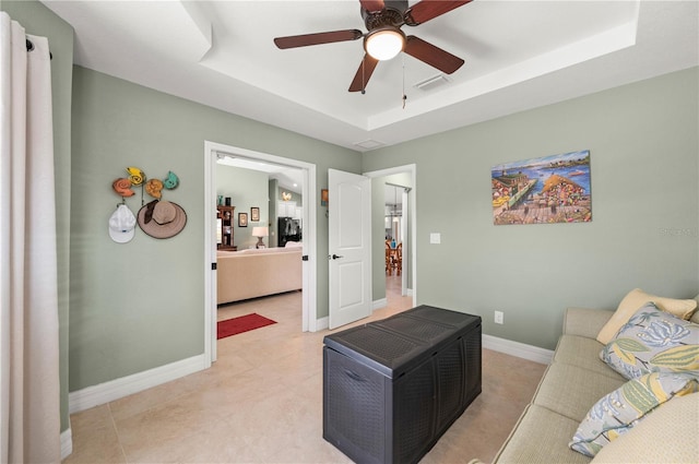 living room with a tray ceiling, baseboards, visible vents, and ceiling fan