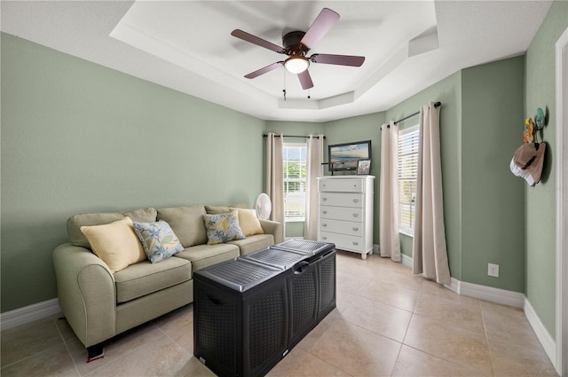 living room featuring a raised ceiling, light tile patterned floors, baseboards, and ceiling fan