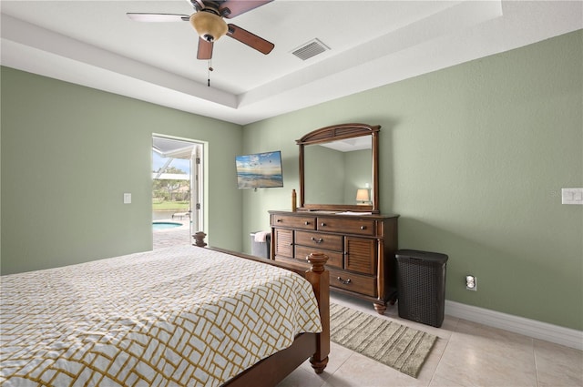 bedroom with visible vents, baseboards, a tray ceiling, light tile patterned flooring, and a ceiling fan