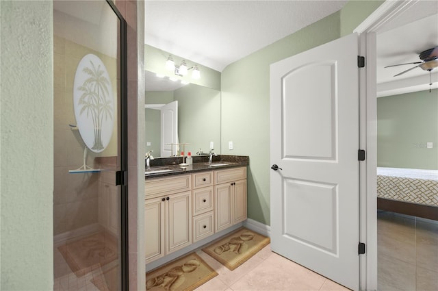 ensuite bathroom with ceiling fan, double vanity, a stall shower, tile patterned floors, and a sink