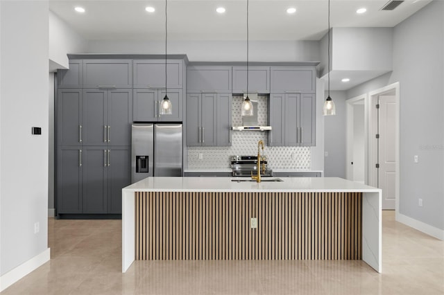 kitchen with gray cabinetry, stainless steel appliances, light countertops, wall chimney range hood, and backsplash