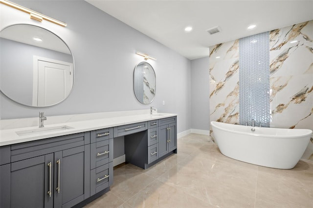 full bathroom with double vanity, a freestanding tub, visible vents, and a sink