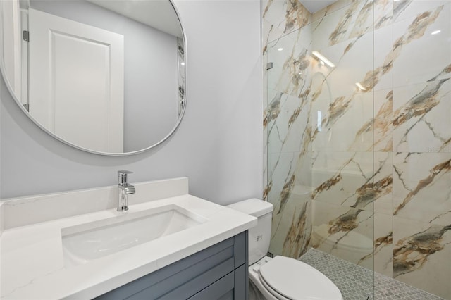 bathroom featuring toilet, a marble finish shower, and vanity