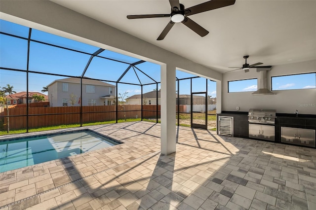 view of pool with glass enclosure, fence, grilling area, and exterior kitchen