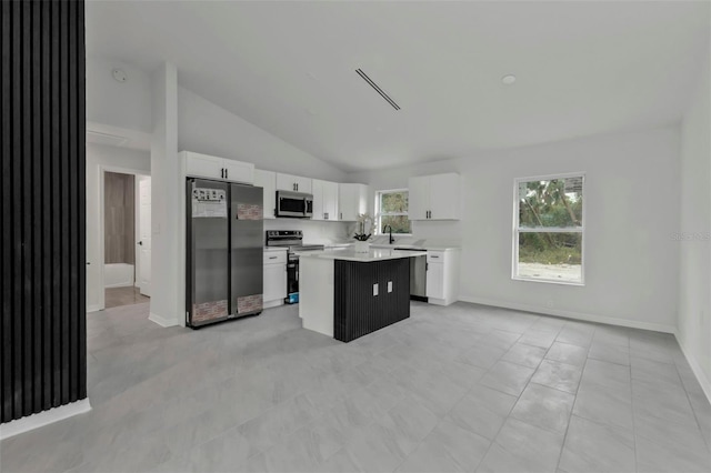 kitchen featuring a center island, white cabinetry, appliances with stainless steel finishes, light countertops, and lofted ceiling