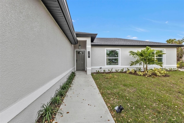 view of exterior entry with stucco siding and a lawn