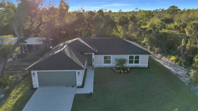 single story home featuring an attached garage, a wooded view, concrete driveway, and a front yard