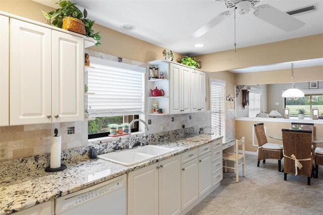 kitchen featuring visible vents, white dishwasher, a sink, white cabinets, and backsplash