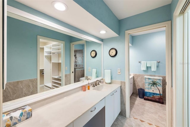 bathroom with a spacious closet, vanity, recessed lighting, wainscoting, and tile walls