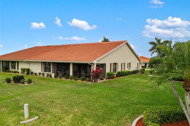 rear view of property featuring stucco siding, a tiled roof, a yard, and a sunroom