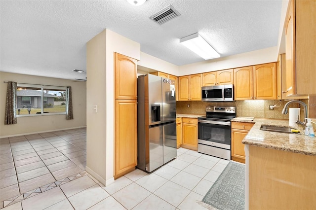 kitchen with a sink, visible vents, appliances with stainless steel finishes, light stone countertops, and tasteful backsplash