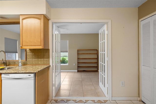 kitchen featuring light tile patterned floors, tasteful backsplash, light stone countertops, white dishwasher, and a sink