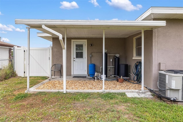 entrance to property featuring central air condition unit, stucco siding, a lawn, a gate, and fence