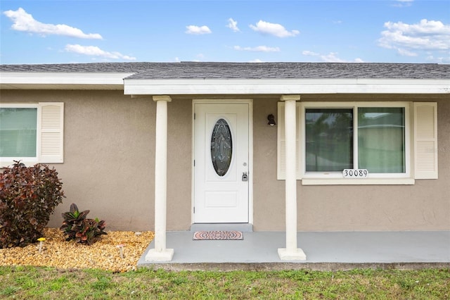 entrance to property featuring a shingled roof and stucco siding