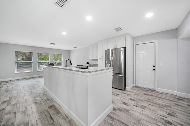 kitchen featuring white cabinets, a center island with sink, visible vents, and stainless steel refrigerator with ice dispenser