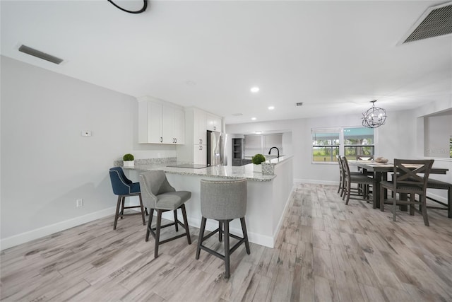kitchen featuring a peninsula, stainless steel fridge, visible vents, and white cabinets