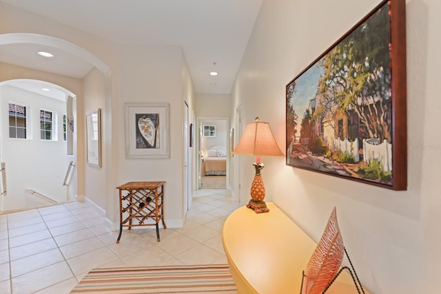 hallway featuring light tile patterned flooring, recessed lighting, arched walkways, and baseboards