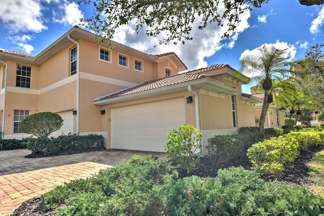 view of property exterior with stucco siding, decorative driveway, an attached garage, and a tile roof