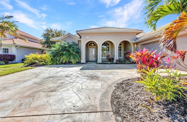 mediterranean / spanish-style house with a garage, stucco siding, driveway, and a tiled roof