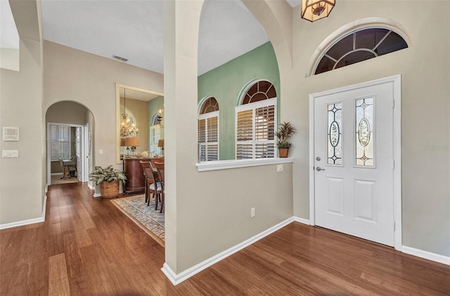 foyer featuring arched walkways, visible vents, a high ceiling, wood finished floors, and baseboards