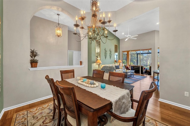 dining space featuring a ceiling fan, a high ceiling, baseboards, and wood finished floors