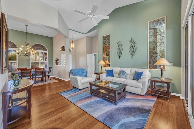 living room featuring baseboards, high vaulted ceiling, wood finished floors, and ceiling fan with notable chandelier