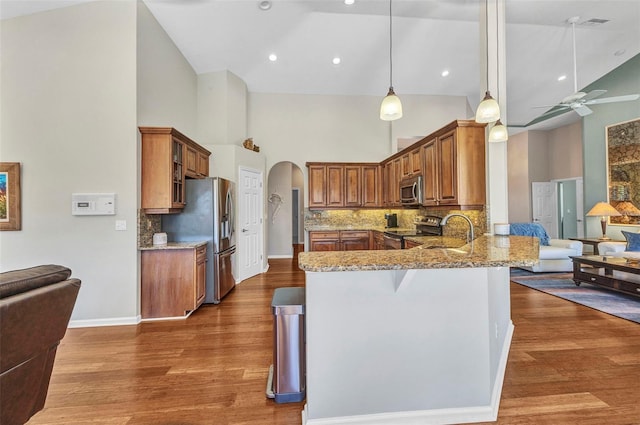 kitchen featuring arched walkways, light stone counters, brown cabinets, a peninsula, and stainless steel appliances