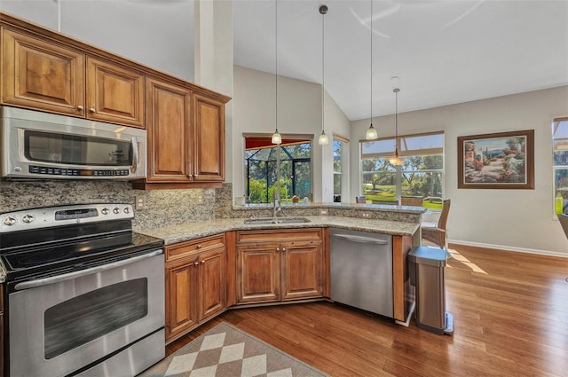 kitchen with light stone countertops, brown cabinetry, stainless steel appliances, and a sink