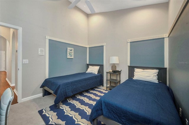 carpeted bedroom featuring baseboards, a high ceiling, arched walkways, and a ceiling fan