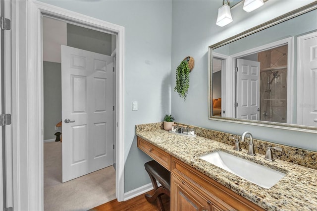 bathroom with tiled shower, vanity, and baseboards