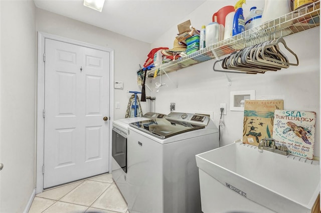 clothes washing area with washing machine and dryer, laundry area, a sink, and light tile patterned floors