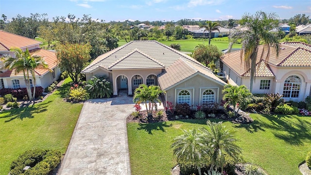 mediterranean / spanish-style house featuring a tile roof, driveway, a front lawn, and stucco siding