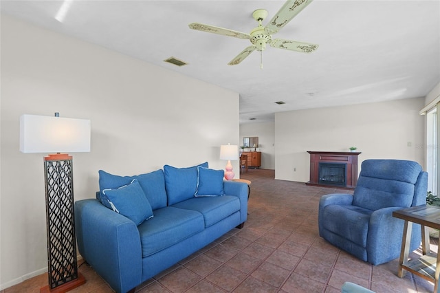 living area with a ceiling fan, visible vents, a fireplace, and dark tile patterned floors