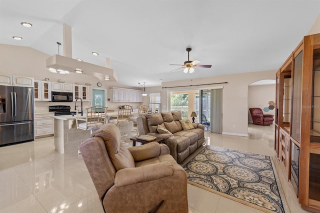 living area with light tile patterned floors, baseboards, arched walkways, ceiling fan, and vaulted ceiling