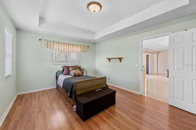 bedroom with baseboards, a raised ceiling, and wood finished floors