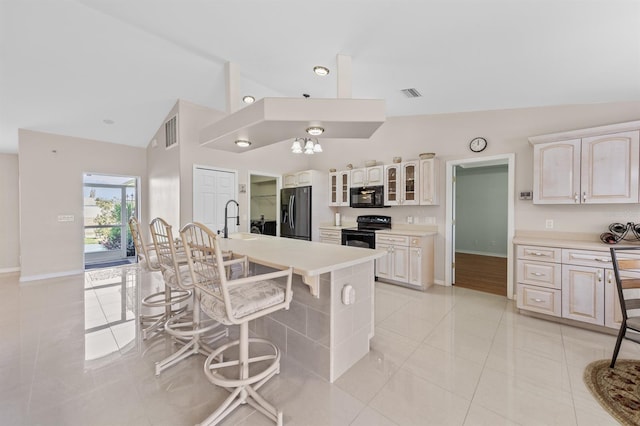 kitchen featuring a breakfast bar area, light countertops, visible vents, glass insert cabinets, and black appliances