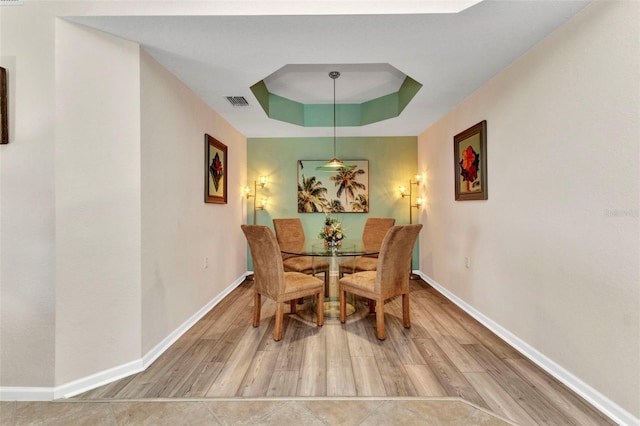 dining space with visible vents, a raised ceiling, baseboards, and wood finished floors