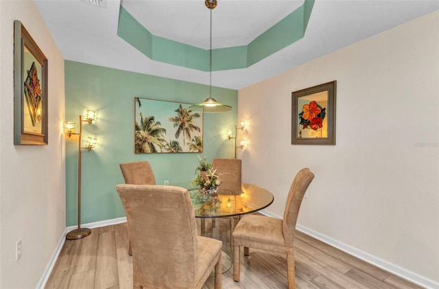 dining area featuring baseboards, a raised ceiling, and wood finished floors