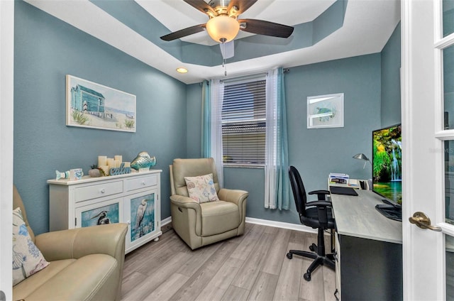 office space featuring ceiling fan, baseboards, a tray ceiling, and wood finished floors