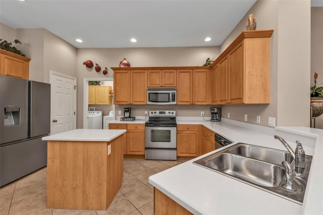 kitchen with washing machine and clothes dryer, a kitchen island, light tile patterned flooring, a sink, and appliances with stainless steel finishes