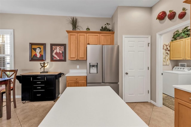 kitchen with light tile patterned floors, baseboards, light countertops, stainless steel fridge, and independent washer and dryer