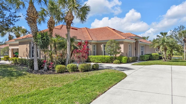 mediterranean / spanish home with a front lawn, concrete driveway, a tile roof, and stucco siding