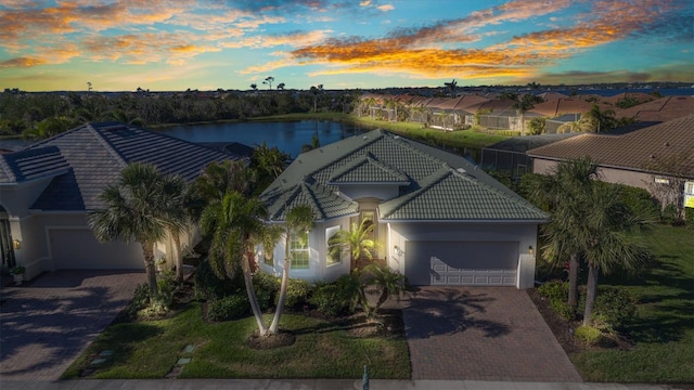 ranch-style house featuring a water view, a tiled roof, stucco siding, decorative driveway, and a garage