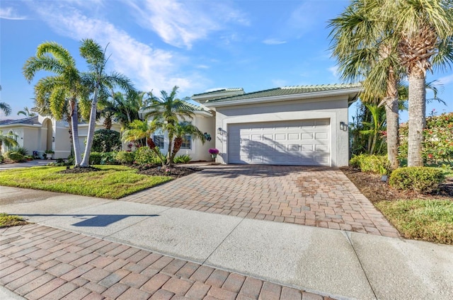 view of front of property featuring stucco siding, a tiled roof, decorative driveway, and a garage