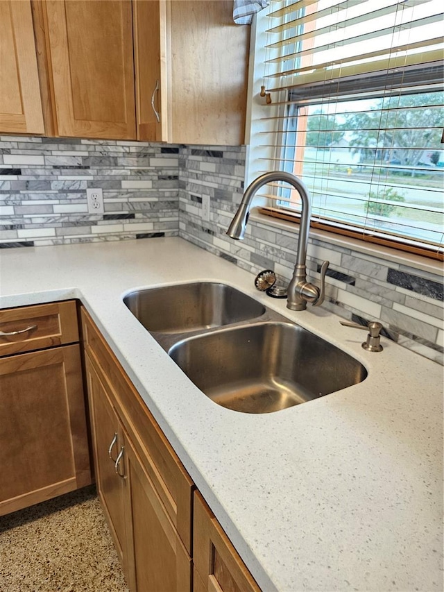 kitchen with light stone counters, backsplash, a sink, and brown cabinetry