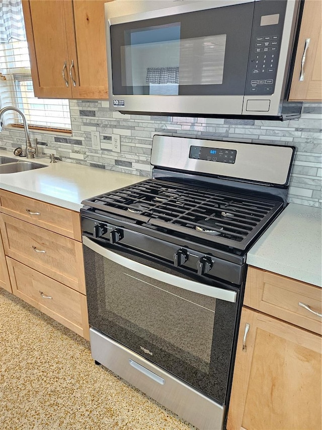 kitchen featuring light countertops, decorative backsplash, appliances with stainless steel finishes, light brown cabinets, and a sink