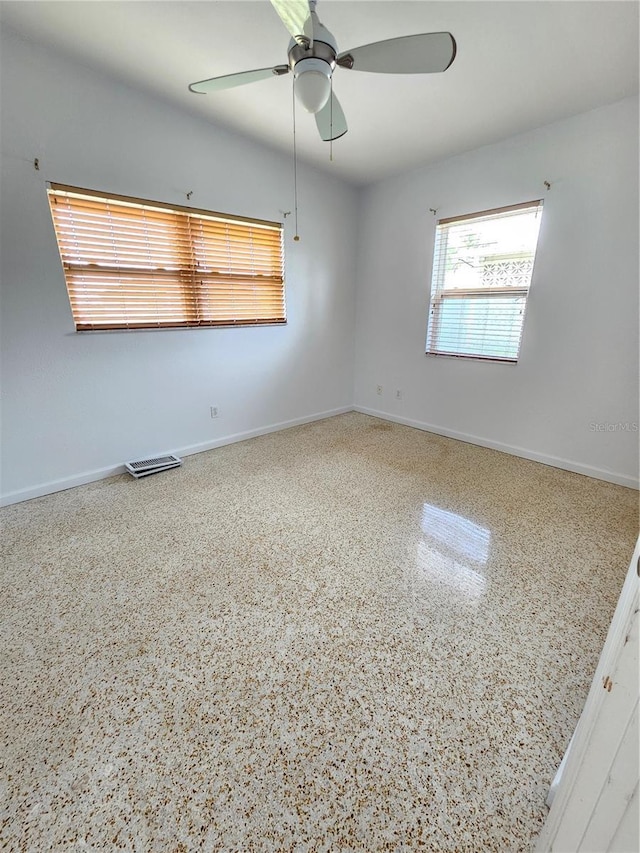 empty room featuring speckled floor, a ceiling fan, and baseboards